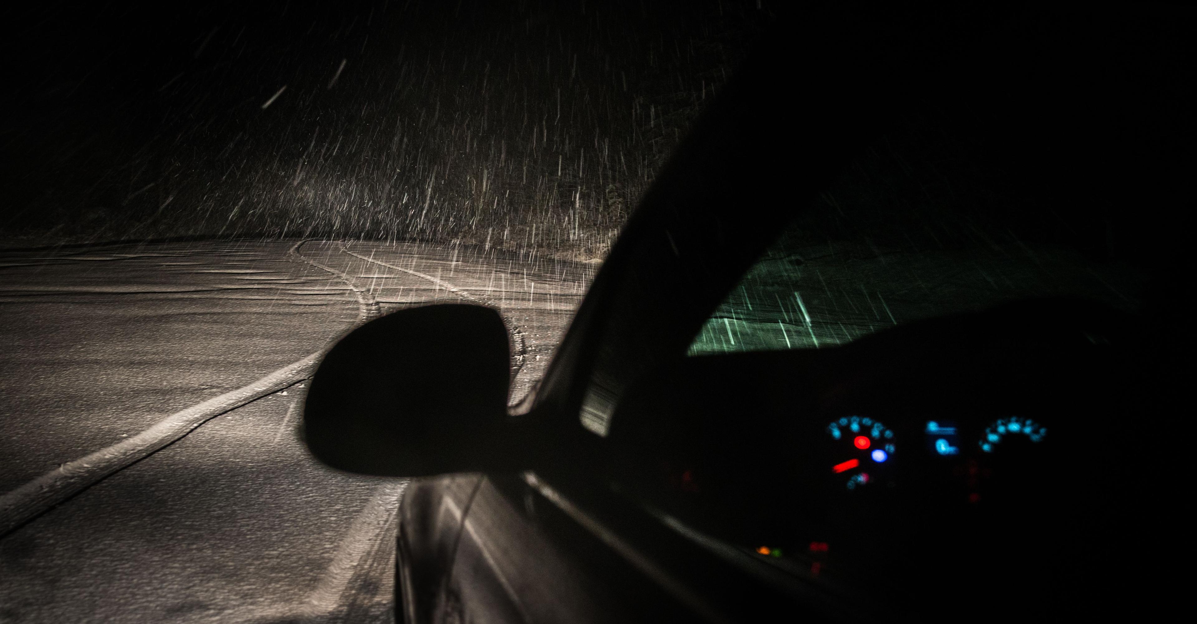 View from inside a car driving a snow-covered road at night, instrument cluster lit